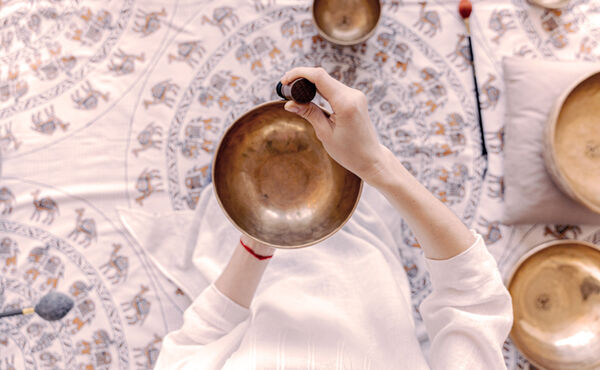 Person holding a Tibetan singing bowl over a patterned cloth, preparing for a calming sound healing session.